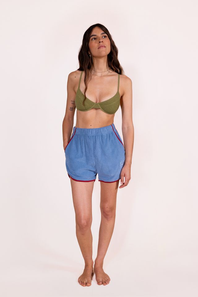Woman wearing a green bikini top and blue shorts on a light pink background