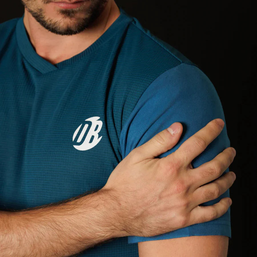 Man wearing a blue shirt with a logo, holding his arm against his chest on a black background