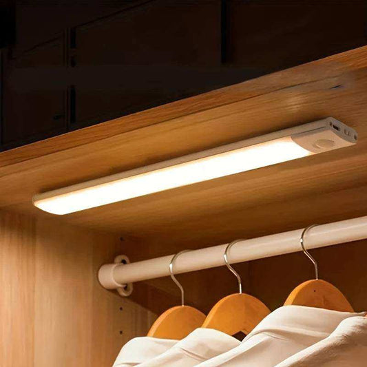 Under-cabinet LED light fixture illuminating a wooden wardrobe with hanging clothes.
