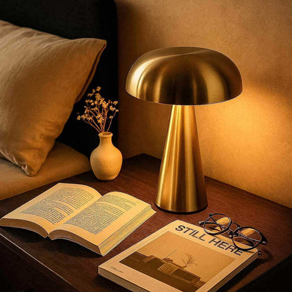 Gold table lamp on a wooden surface with an open book and glasses nearby.