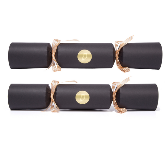 Two black Christmas crackers with gold ribbons and a gold button on a white background