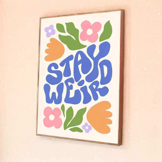 Framed artwork with 'Stay Weird' text and colorful flowers on a beige wall.