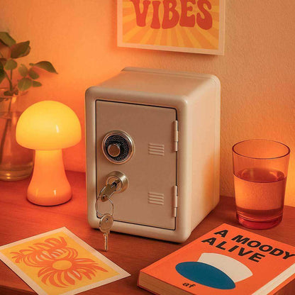 Small beige safe on a wooden surface with a glowing lamp, plant, and book in a warm setting.