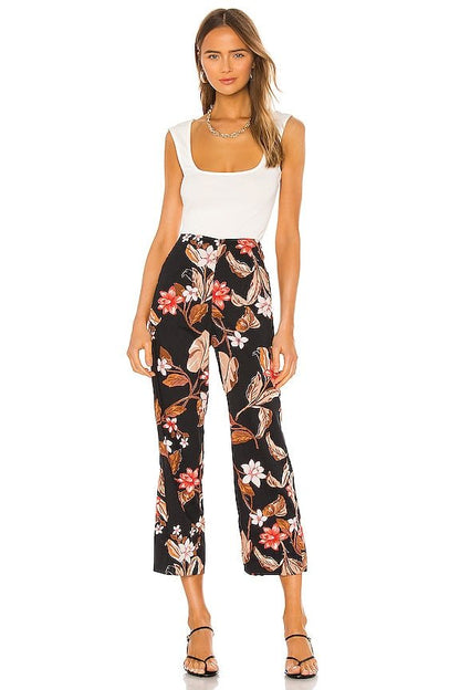 Woman wearing a white top and black floral pants on a white background