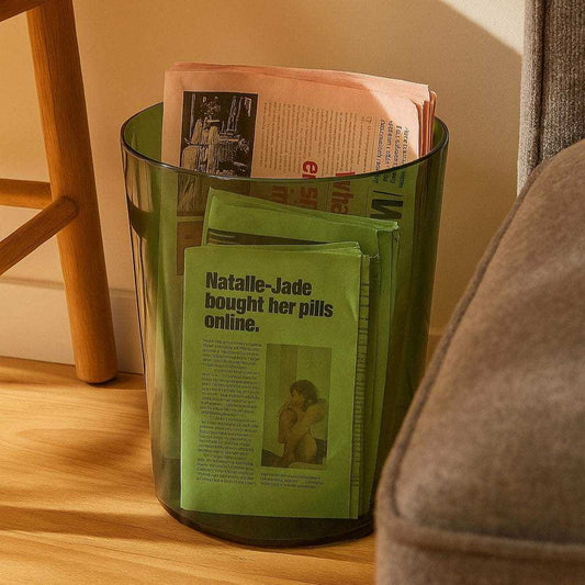 Green trash bin with newspapers inside on a wooden floor.