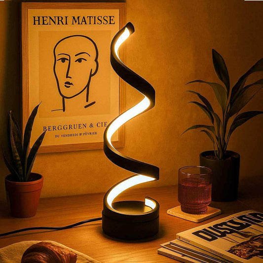 Spiral lamp on a table with a plant, glass, and book in a warm setting