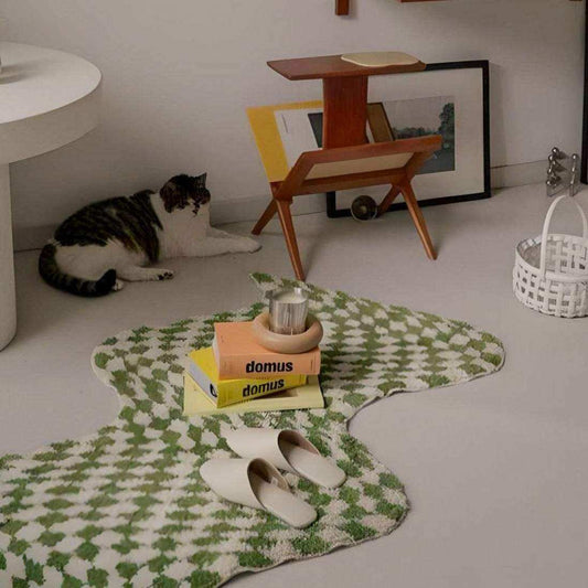 Cat lying on a green patterned rug with books and a candle in a room.