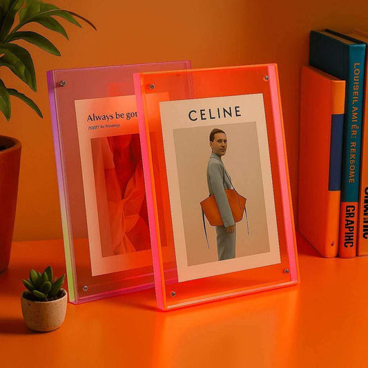 Two neon pink picture frames on an orange surface with books and a plant in the background.