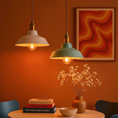 Two pendant lights hanging above a table with books and a vase against an orange wall with a colorful abstract painting.