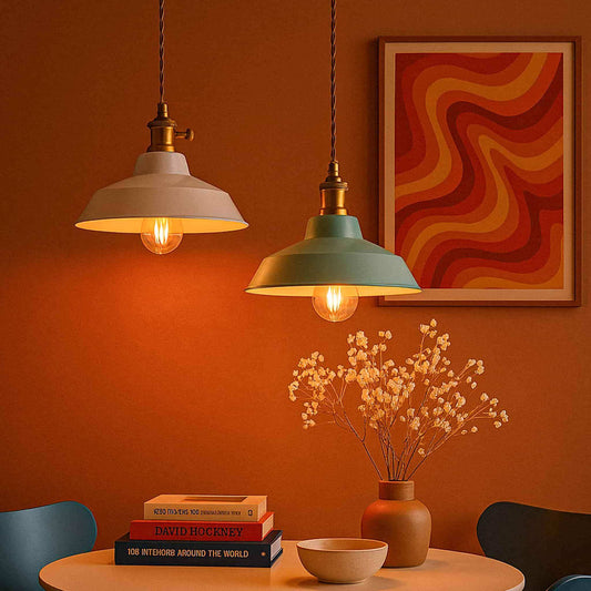 Two pendant lights hanging above a table with books and a vase against an orange wall with a colorful abstract painting.