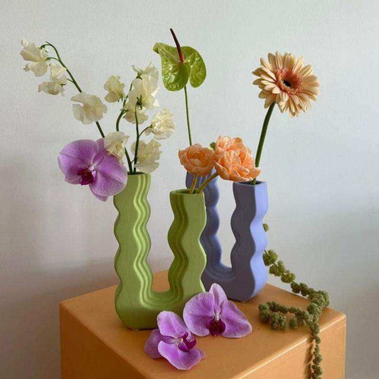 Three wavy-patterned vases with flowers on a wooden surface against a light background