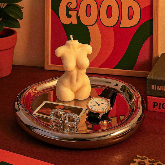Decorative tray with a candle, clock, and small sculptures on a wooden surface with a colorful abstract painting in the background.